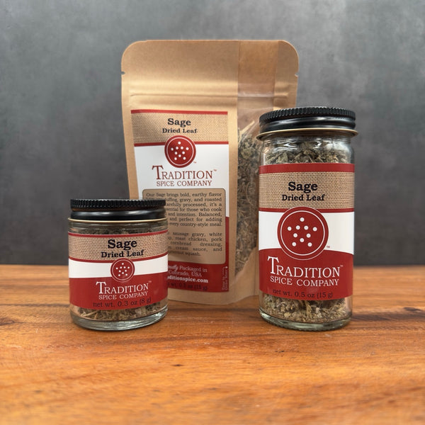 Two jars and a package of sage dried leaf from Tradition Spice Company on a wooden surface with a gray background.