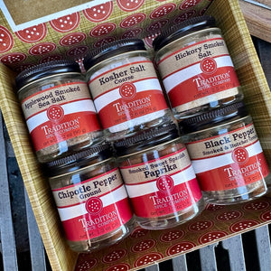A gift box containing six jars of spices and seasonings, including smoked sea salt, kosher salt, hickory smoked salt, chipotle pepper, paprika, and black pepper.