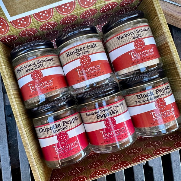 A gift box containing six jars of spices and seasonings, including smoked sea salt, kosher salt, hickory smoked salt, chipotle pepper, paprika, and black pepper.