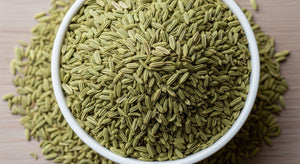 A white bowl filled with Whole Fennel Seed, a classic ingredient in Italian sausage seasoning, with extra seeds scattered around the bowl on a light wooden surface.