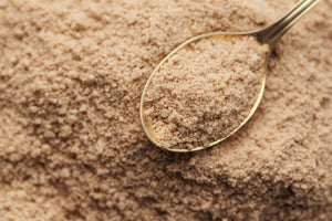 A metal spoon scoops light brown, finely ground Hickory Smoked Salt from a pile—ideal for enhancing your next Bloody Mary or adding bold wood-fired smokehouse flavor to any dish.