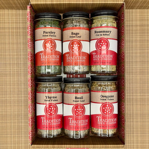 The Basic Herbs - Pantry Pack 2 includes six jars of parsley, sage, rosemary, thyme, basil, and oregano, each labeled with the Tradition Spice Company brand and herb name and neatly arranged in a box.