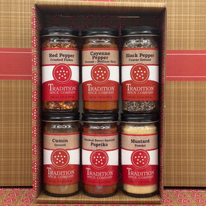 The Basic Spices - Pantry Pack 2 is a gift box with six clear jars of essential cooking spices—red pepper flakes, cayenne pepper, black pepper, cumin, smoked sweet Spanish paprika, and mustard powder—with red and white labels.