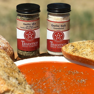 Two jars of garlic seasoning from Tradition Spice Company with bread and soup in the background.