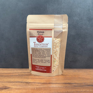 A stand-up pouch of Tradition Spice Company Onion Minced spice mix, displayed on a wooden surface against a dark gray background.