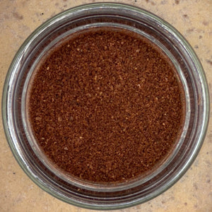 A glass jar of finely ground cloves rests on a beige countertop, viewed from above.