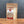 A stand-up kraft paper pouch of Tradition Spice Company Garlic Powder, standing on a wooden surface against a dark gray textured background.