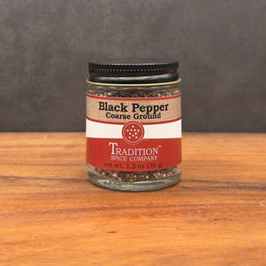 A 1.3 oz (36 g) glass jar of Course Ground Black Pepper sits on a wooden surface against a dark background, ready to add bold, rustic flavor to any dish.