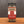 A glass jar of Restaurant Style Black Pepper with a black lid rests on a wooden surface against a dark background. The tan and red label displays white and black text, highlighting its bold seasoning flavor.