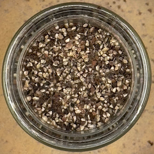 A glass jar of Restaurant Style Black Pepper features coarse, crushed pepper pieces in black, brown, and off-white hues, offering bold flavor seasoning.