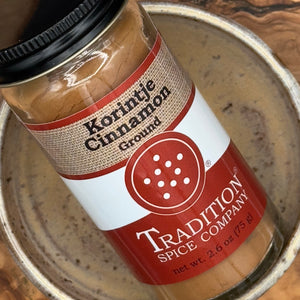 A jar of Ground Saigon Cinnamon from Tradition Spice Company sits on a ceramic plate, displaying its rich brown spice through the clear container—a perfect addition to your collection of baking spices.