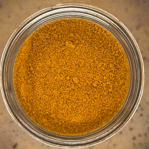 A top-down view of a fine yellow-orange powder, likely turmeric or curry powder, inside a clear glass jar.