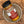 A glass jar of Tradition Spice Company Turmeric Ground spice, featuring a black lid and a label with red, white, and burlap textures, resting inside a small ceramic dish on a wood grain surface.