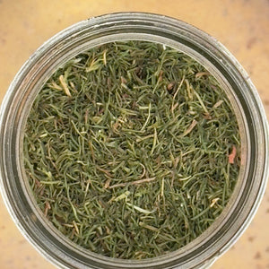 A top-down view of loose green tea leaves inside a clear glass jar, set against a warm yellow-beige background.