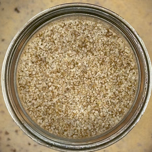 Top-down view of coarse sea salt granules inside a clear glass jar with a metal rim, set against a textured beige background.