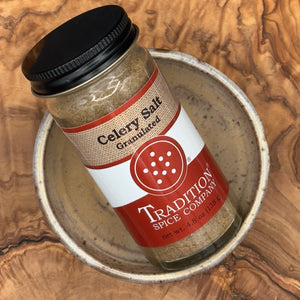 A jar of Tradition Spice Company Celery Salt Granulated, resting inside a rustic metal bowl.