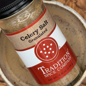 A close-up of a jar of Tradition Spice Company Celery Salt Granulated, resting inside a rustic metal bowl.