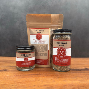 Three Whole Dill Seed containers are shown on a wooden surface against a gray background: a small glass jar, a plastic pouch, and a large glass jar, each with red and white labels.