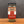A glass jar of Tradition Spice Company Marjoram Dried Leaf on a wooden surface against a dark gray textured background.