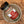 A glass jar of Tradition Spice Company Marjoram Dried Leaf seasoning with a black lid and red-and-white label, resting inside a small ceramic dish on a wood grain surface.