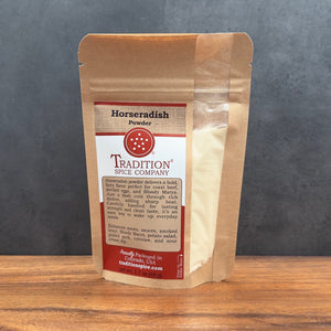 A stand-up pouch of Tradition Spice Company Horseradish Powder, filled with pale beige powder, set on a wooden surface against a dark gray background.