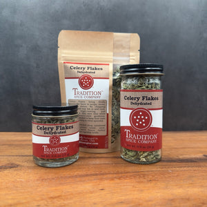 Three jars and pouches of Dehydrated Celery Flakes are displayed on a wooden surface, highlighting their garden-fresh flavor against a gray background.