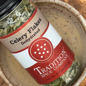 A jar of Dehydrated Celery Flakes sits angled on a ceramic bowl, ready to deliver garden-fresh flavor to every dish.