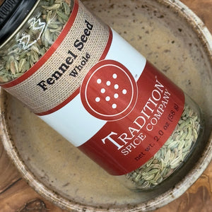 A jar of Whole Fennel Seed sits in a ceramic bowl, displaying the red and tan label with name, logo, and 2 oz net weight. The visible seeds are perfect for Italian sausage seasoning or adding flavor to rustic breads.