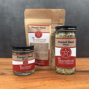 Three containers of Whole Fennel Seed—a small glass jar, a larger glass jar, and a labeled brown resealable pouch—are arranged on a wood surface. Ideal for seasoning Italian sausage or adding flavor to rustic breads.
