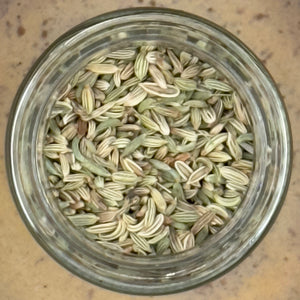 A glass jar of Whole Fennel Seed, seen from above on a brown surface—ideal for enhancing Italian sausage seasoning or rustic breads.