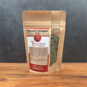 A brown paper pouch of French Tarragon sits on a wooden surface, featuring a clear window that reveals the herb and a red and white label with product details.
