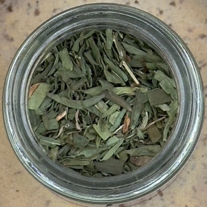 A glass jar of French Tarragon dried leaves, seen from above on a beige surface—ideal for enhancing your favorite dishes with the unique, classic flavor of this beloved cooking herb.