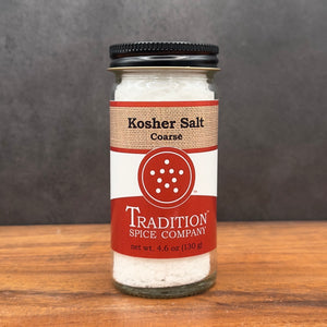 A glass jar of Coarse Kosher Salt rests on a wooden surface, showing off its red and beige label with dotted circle design and a black twist-off lid—ideal as your everyday cooking salt.