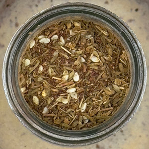 A close-up, top-down view of Za’atar, Worldly Wow! Middle Eastern Blend—a glass jar filled with a coarse mix of dried herbs, visible sesame seeds, and tangy sumac spice.