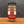 A glass jar of Tradition Spice Company Dukkah Worldly Woul Egyptian Blend spice, featuring a red and white label with a burlap-textured band, set on a wooden surface against a dark gray background.