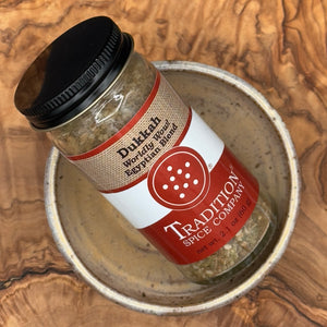 A jar of Tradition Spice Company Dulketh Worldly Wound Bay Leaf Blend spice seasoning, resting on a ceramic plate over a rustic wood grain surface.