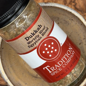 A close-up of a spice jar labeled 'Dikkah Worldly Mowd Egyptian Blend' by Tradition Spice Company, resting inside a metal bowl.