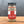 A glass jar of Sizzl’n Lime, Da Best! Chili Lime Seasoning sits on a wooden surface with a gray background. The jar, filled with zesty chili lime spice, has a black lid and a bold red and white label.