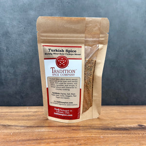 A brown resealable pouch of Turkish Spice, Worldly Wow! Bold Türkiye Blend stands on a wooden surface. The front label lists ingredients, describes the blend, and features contact details at the bottom.