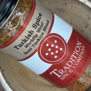A jar of Turkish Spice, Worldly Wow! Bold Türkiye Blend sits on a ceramic dish—a bold seasoning, perfect as a lamb rub or for adding Turkish-inspired flavor to your favorite dishes.