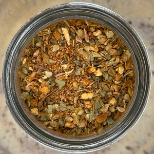 A close-up, top-down view of a jar filled with Turkish Spice, Worldly Wow! Bold Türkiye Blend, showing green and brown flakes and small orange-brown pieces.