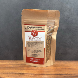 A stand-up pouch of Tradition Spice Company Turkish Spice on a wooden surface against a dark gray background.