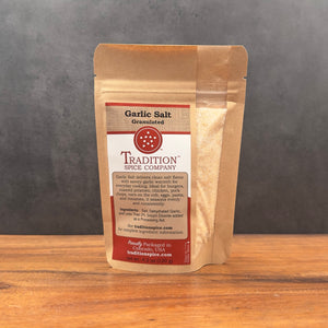 A brown resealable pouch labeled Granulated Garlic Salt rests on a wooden surface, displaying details and ingredients on the front.