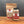 A brown paper bag and a clear glass jar of Granulated Garlic Salt sit side by side on a wood surface against a gray background, both featuring red and white labels.