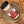 A jar of Granulated Garlic Salt sits at an angle in a speckled ceramic bowl on a wooden surface, ready to enhance any dish with savory flavor.