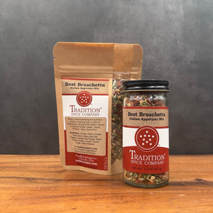 A jar and stand-up pouch of Tradition Spice Company Best Bruschetta Italian Appetizer Mix displayed on a wooden surface against a dark gray background.