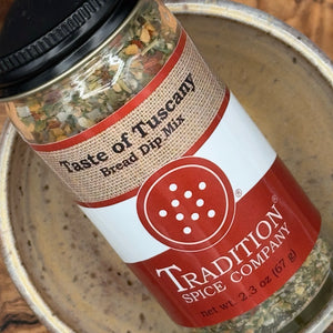 A jar of Tradition Spice Company Taste of Tuscany Bread Dip Mix placed inside a ceramic bowl, showing the product label and visible dried herbs inside the clear container.