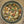 Top-down view of a clear glass jar filled with a colorful dried herb and spice blend containing chopped nuts, seeds, leaves, and small orange pieces, set on a beige textured surface.