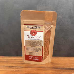 A stand-up pouch of Tradition Spice Company 'Slice of Sicily' bread dip mix, shown on a wooden surface against a dark gray background.