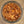 A top-down view of a clear glass jar filled with a textured, granular brown and orange mixture resembling bark, wood chips, or a natural spice blend, set against a speckled beige countertop.